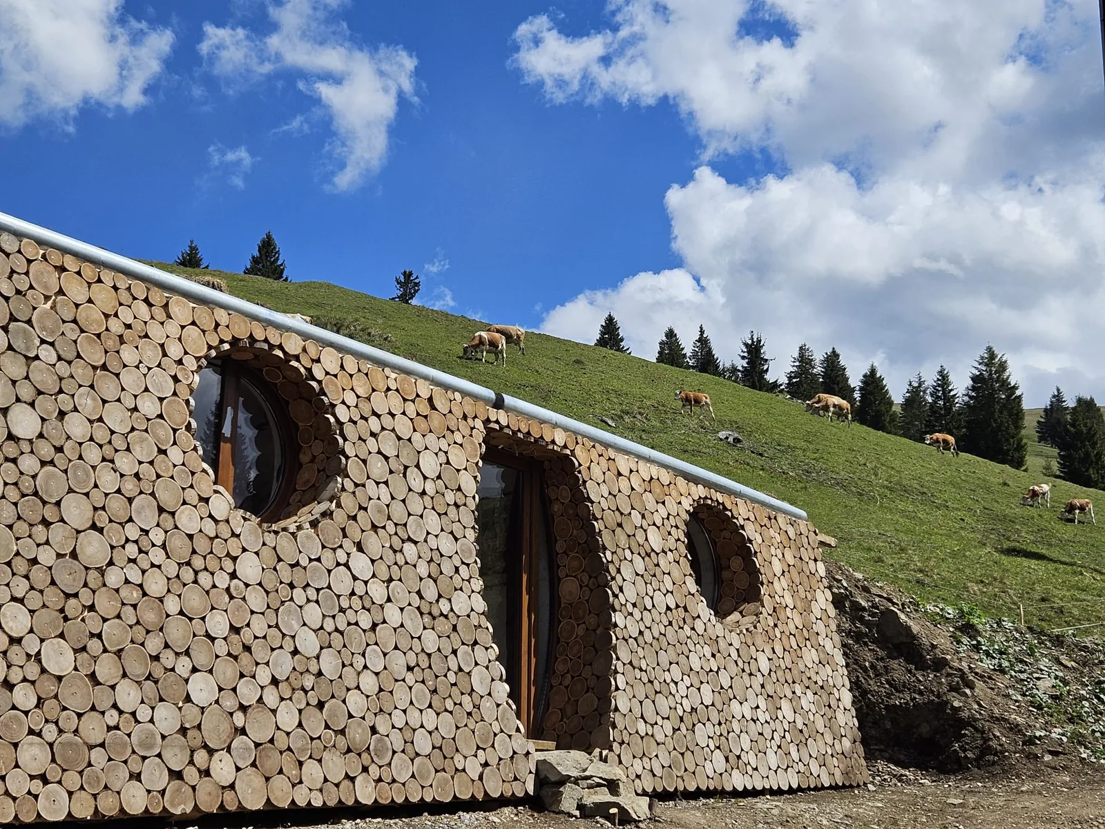 A zöld domboldalba épített Hobbitlak farönk homlokzata, körablakai és bejárata